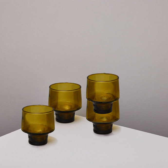 Three amber-brown translucent stacking glass tumblers, arranged on a white surface against a plain light gray wall.