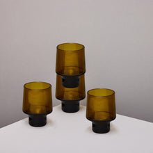 Four amber-brown translucent stacking glass tumblers, arranged on a white tabletop against a plain light gray wall.
