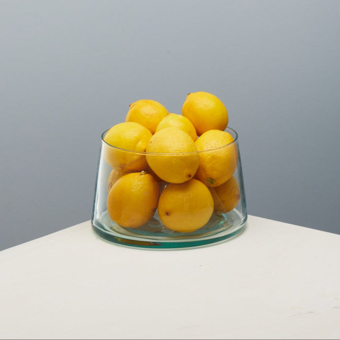 Handmade Glass bowl filled with lemons on a white surface with a gray background